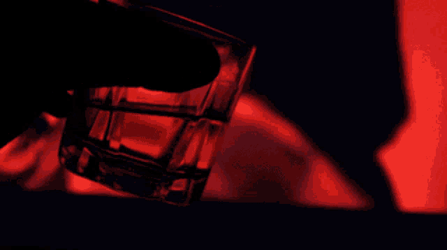 a person is holding a shot glass with a red light behind them