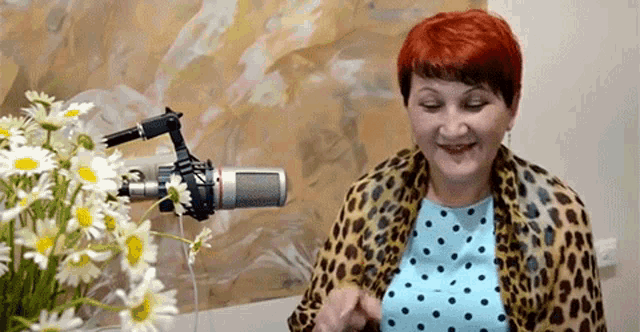 a woman is smiling in front of a microphone in front of a vase of daisies .