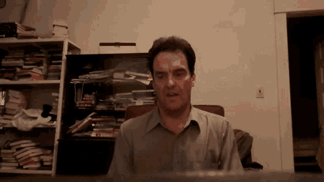a man is sitting in front of a bookshelf with a stack of books on it