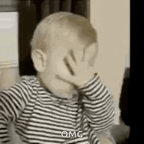 a baby is covering his face with his hand and saying `` omg '' .